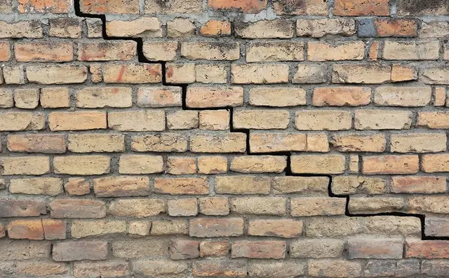 Ground Up Foundation Repair, Waterproofing and Concrete Leveling inspecting stair-step crack in brick foundation.