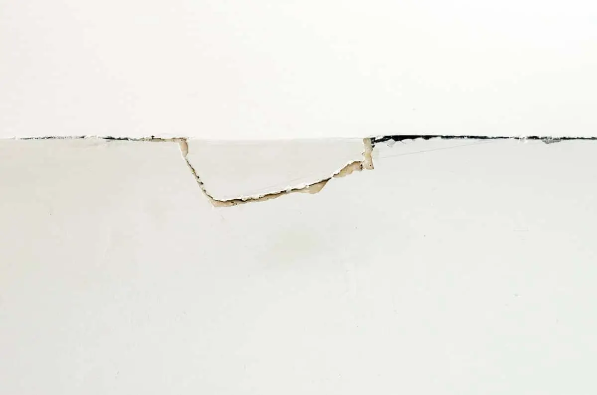 A crack where the wall meets the ceiling with peeling drywall.