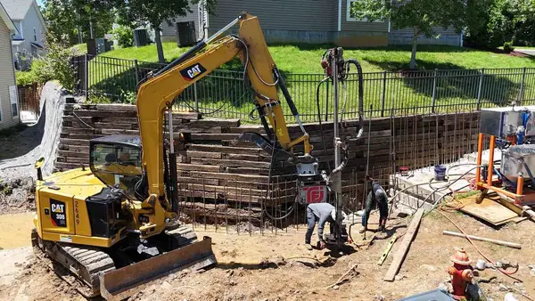 A commercial crew performing foundation and retaining wall repair with heavy equipment.