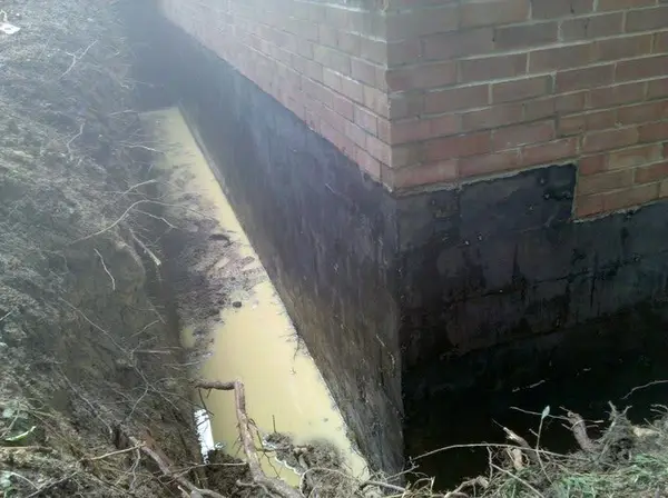 Standing water pooling in an exterior foundation trench due to poor drainage.