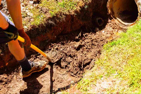 A worker digging a trench for French drain pipe installation.