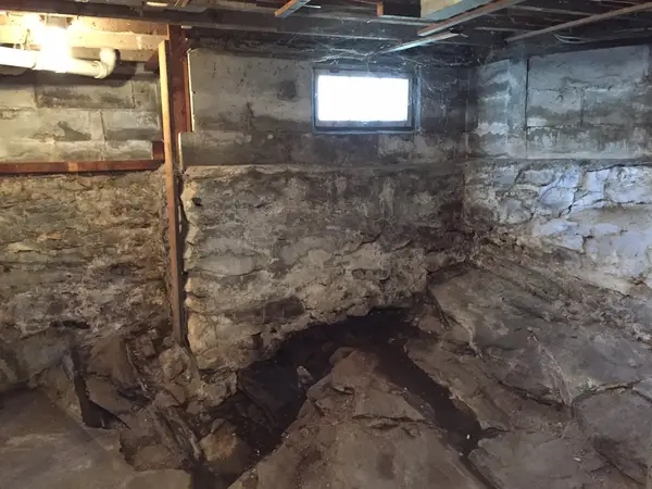 Inspecting a cracked stone and concrete block basement foundation.