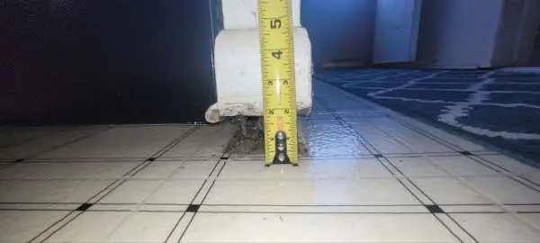 Using a measuring tape to check floor settlement above a crawl space support post.