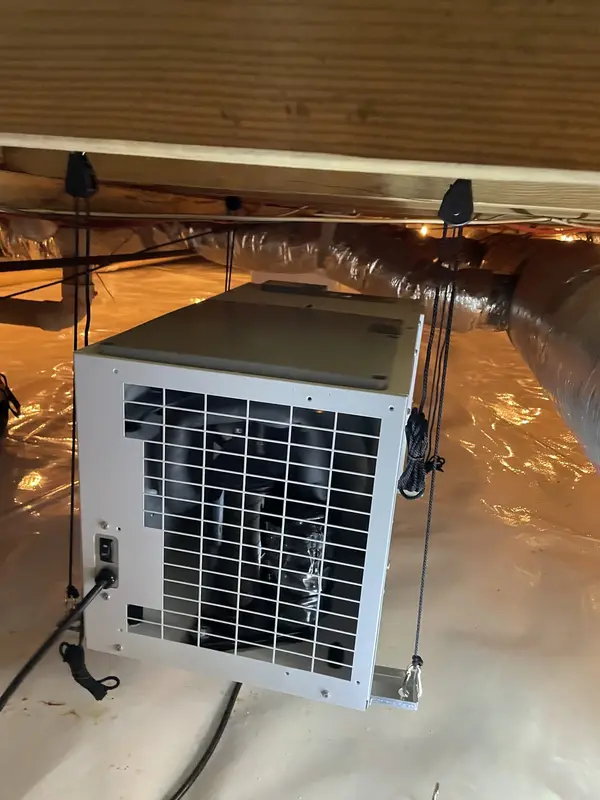A crawl space dehumidifier installed and hanging beneath the floor framing.