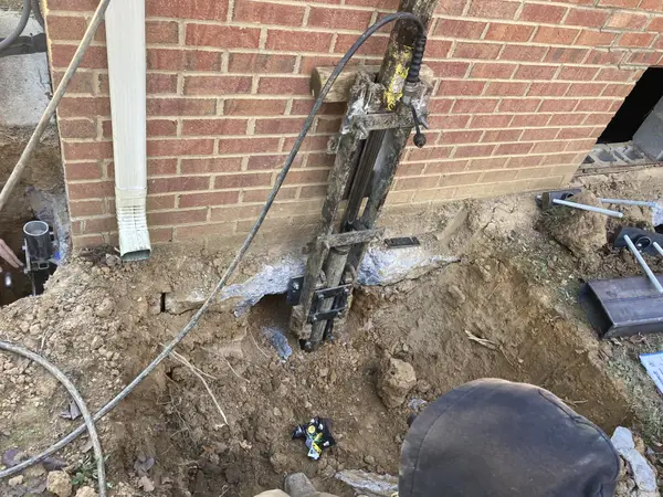 Installing a foundation pier with a hydraulic ram against an exterior brick foundation wall.