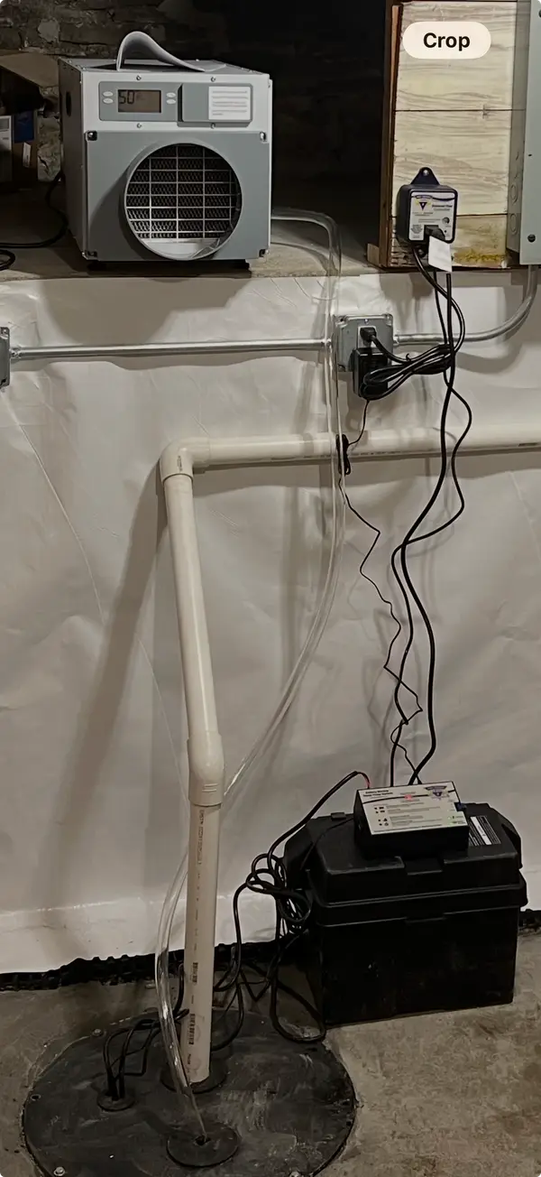 A battery backup sump pump system installed beside the sump basin in a crawl space.